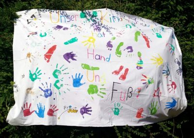 Ein großes weißes Tuch mit bunten Hand- und Fußabdrücken